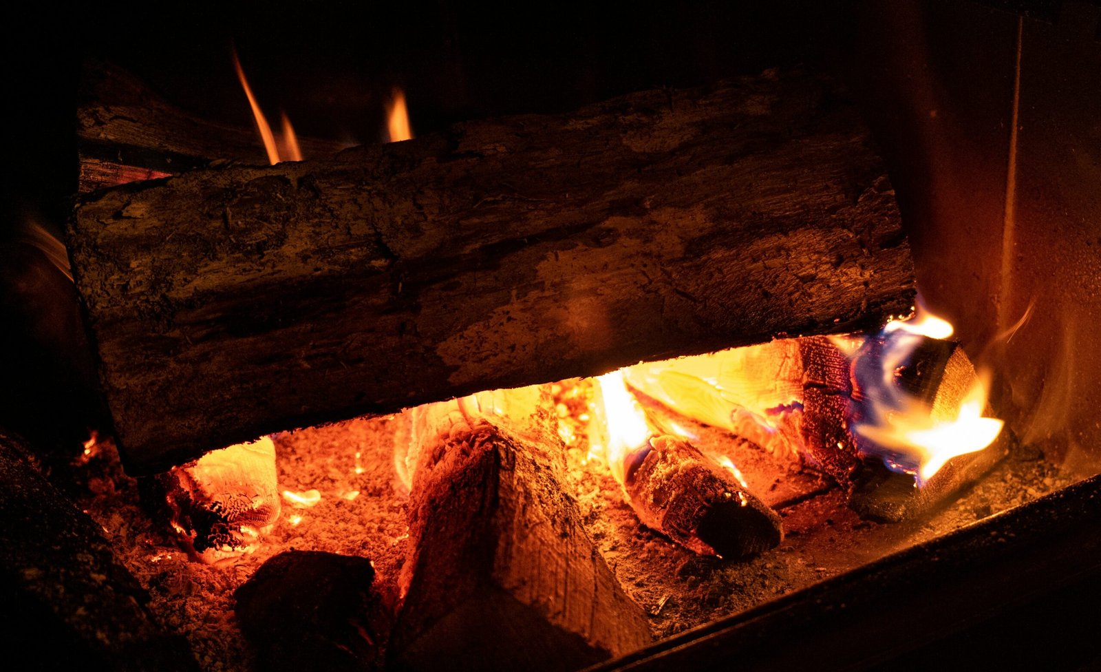 Close-up of burning logs in a fireplace, showing glowing embers and bright orange flames.